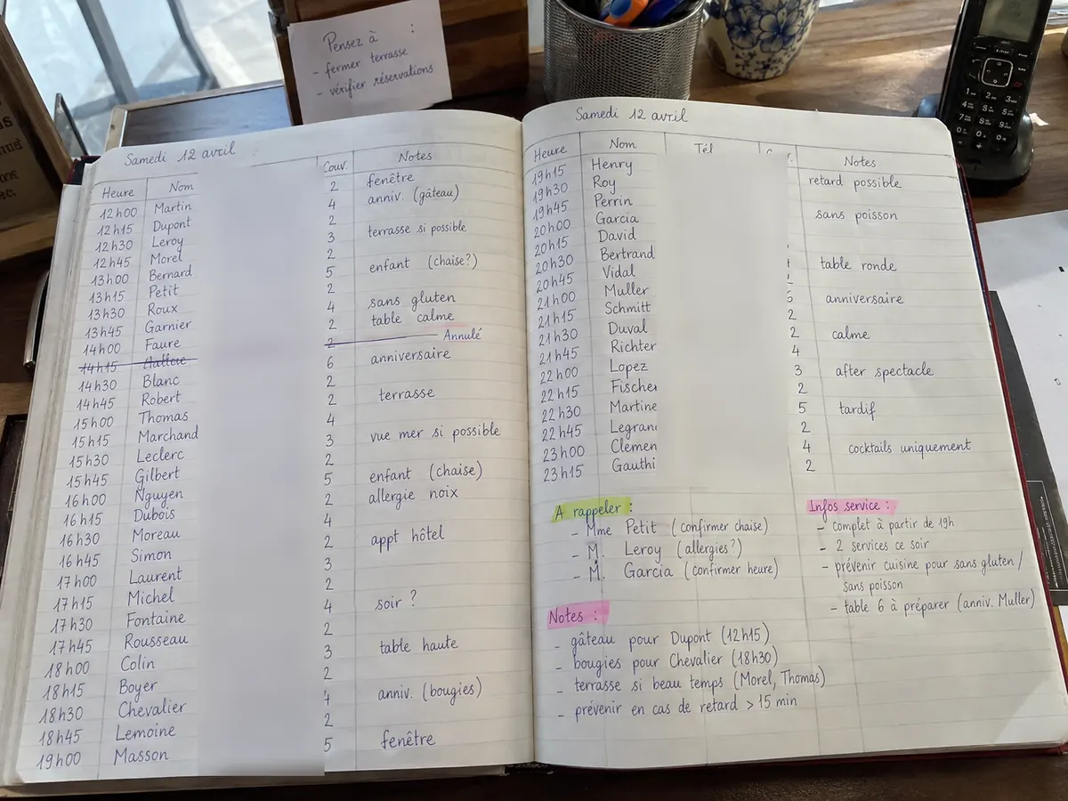 Un cahier de réservations tenu à la main : noms, téléphones, notes et ratures